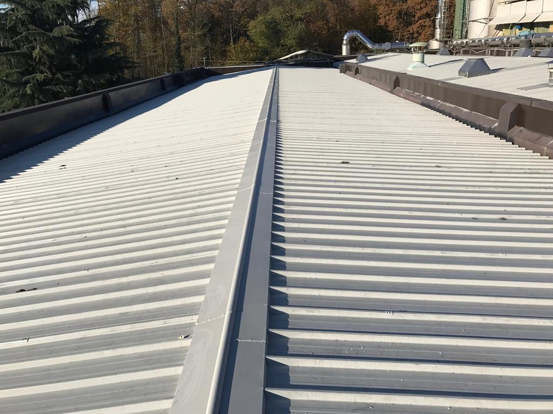 Copertura industriale rifatta con lastre grecate chiare e colmo in lamiera, dopo la bonifica